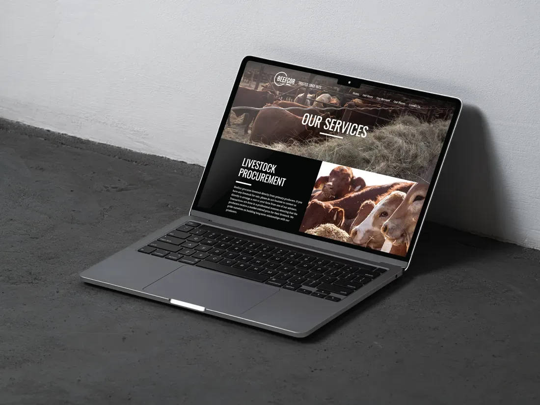 Laptop on a concrete floor showing the Beefcor website services page with black-and-white farm photography.