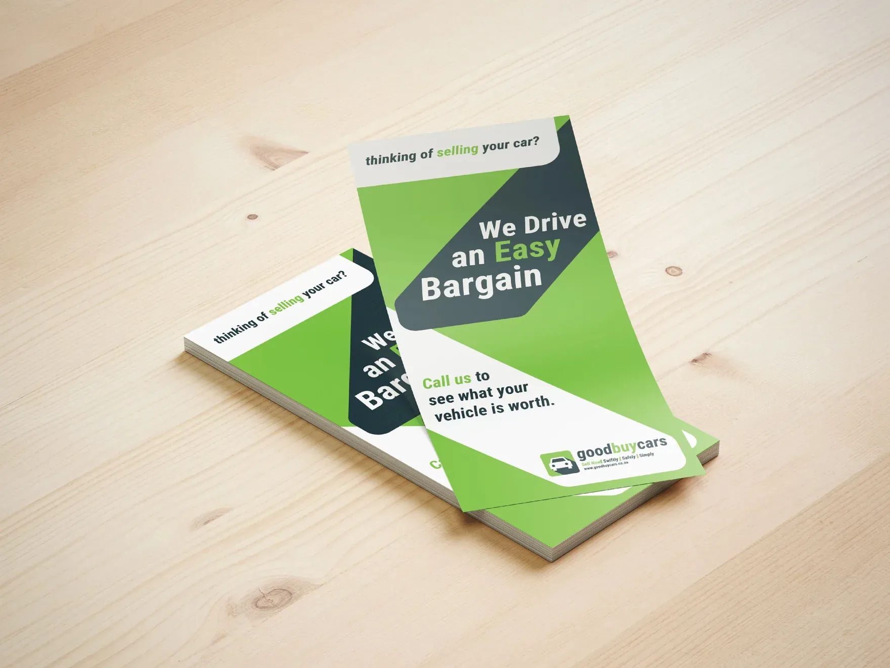 Stack of Good Buy Cars leaflets reading We Drive an Easy Bargain on a wooden table.